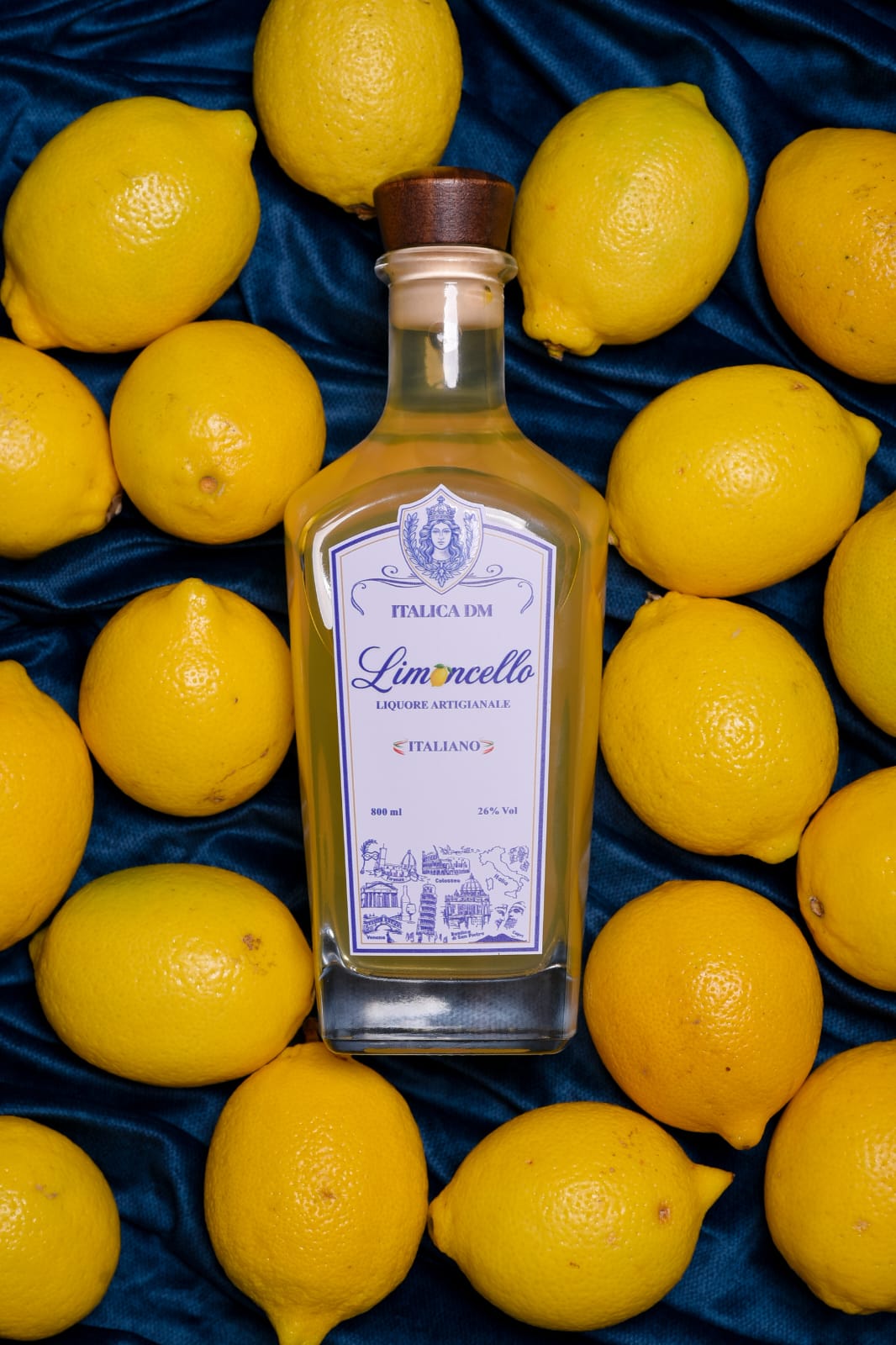 Garrafa de Limoncello Italica DM cercada de limões sicilianos sobre veludo azul