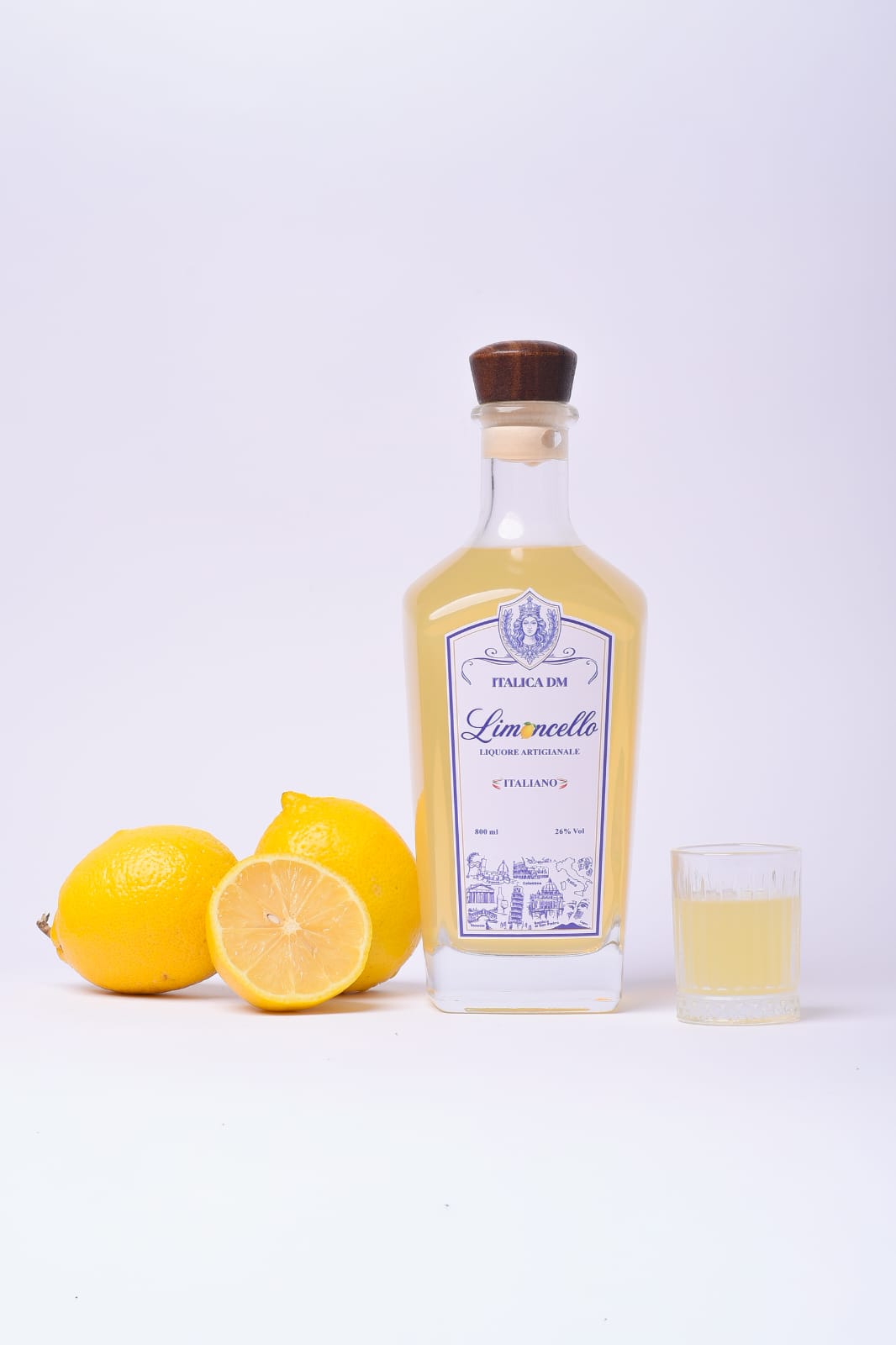 Garrafa de Limoncello Italica DM em estúdio claro, com limões e um cálice